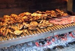 This image show a variate of meat being cooked asado style on a Argentine Parrilla BBQ