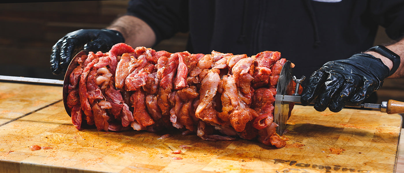 Stacked marinated gyros meat evenly threaded onto a rotisserie skewer on a cutting board ready for cooking.