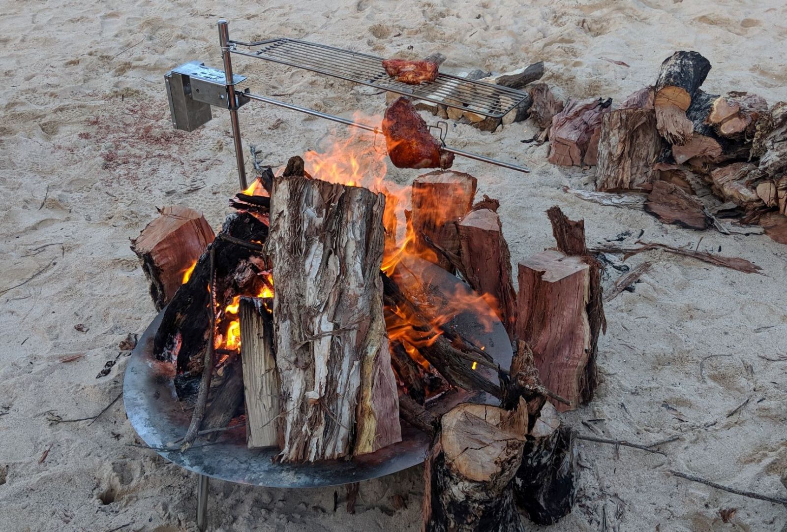 This image show the Auspit Portable camping grill being used along with the auspit rotisserie above an open camp fire