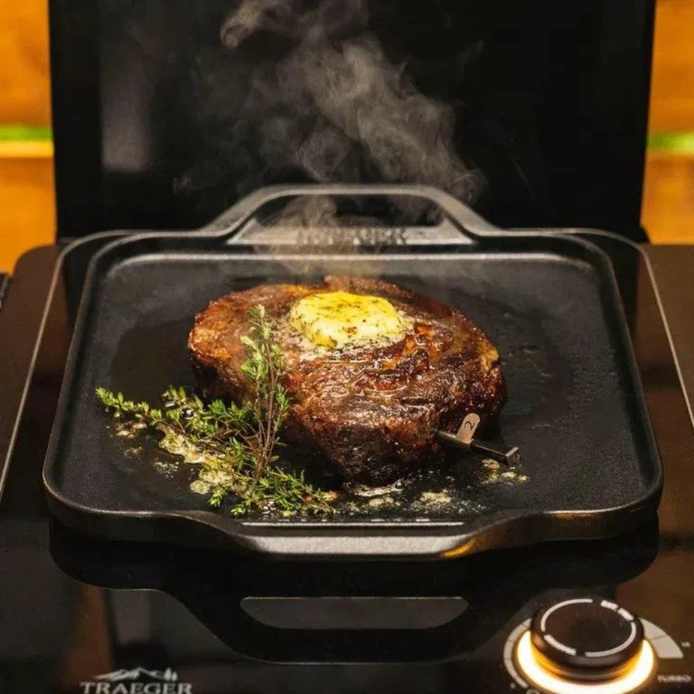 Traeger induction cast iron skillet searing steak with butter and herbs