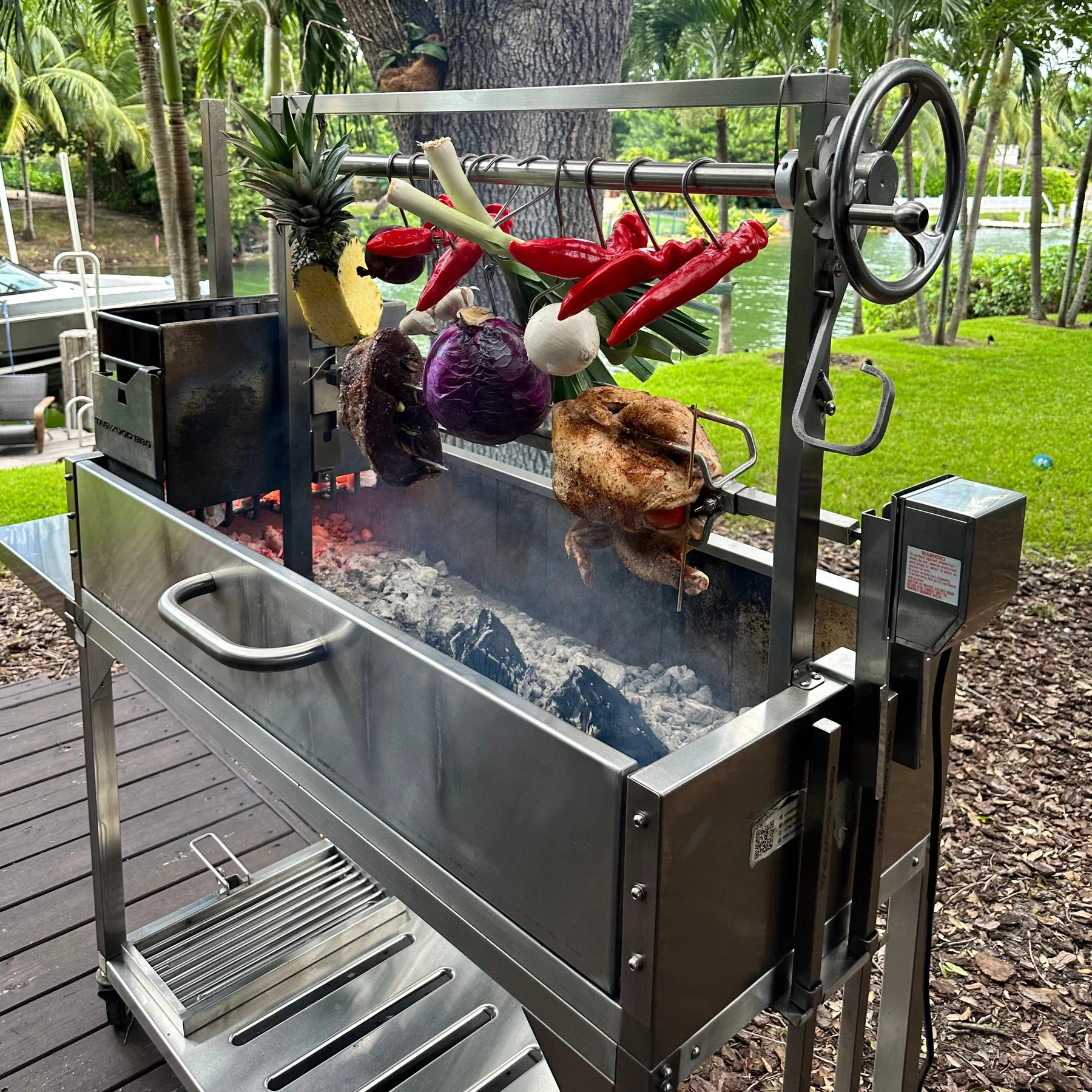 Tagwood stainless steel parrilla BBQ rotisserie kit cooking whole chicken and vegetables over charcoal