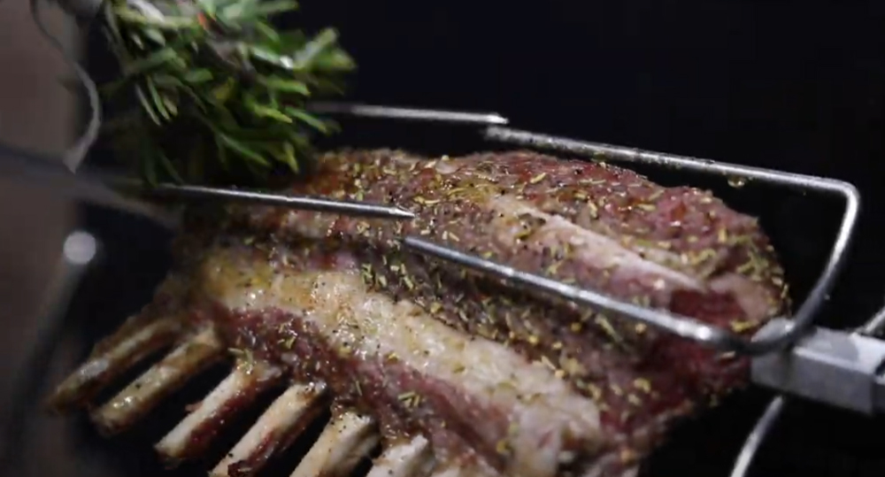 This_image_shows_lamb_rack_being_basted_with_olive_oil_using_rosemary_sprig