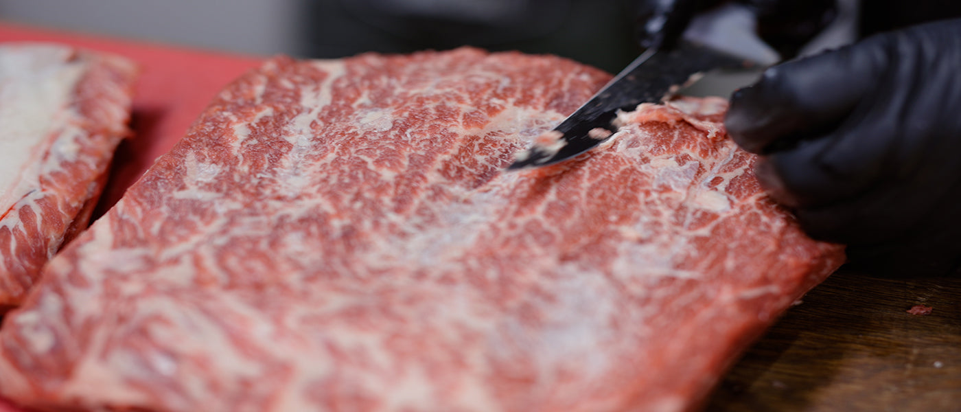 This image shows a man trimming the fats of beef short ribs