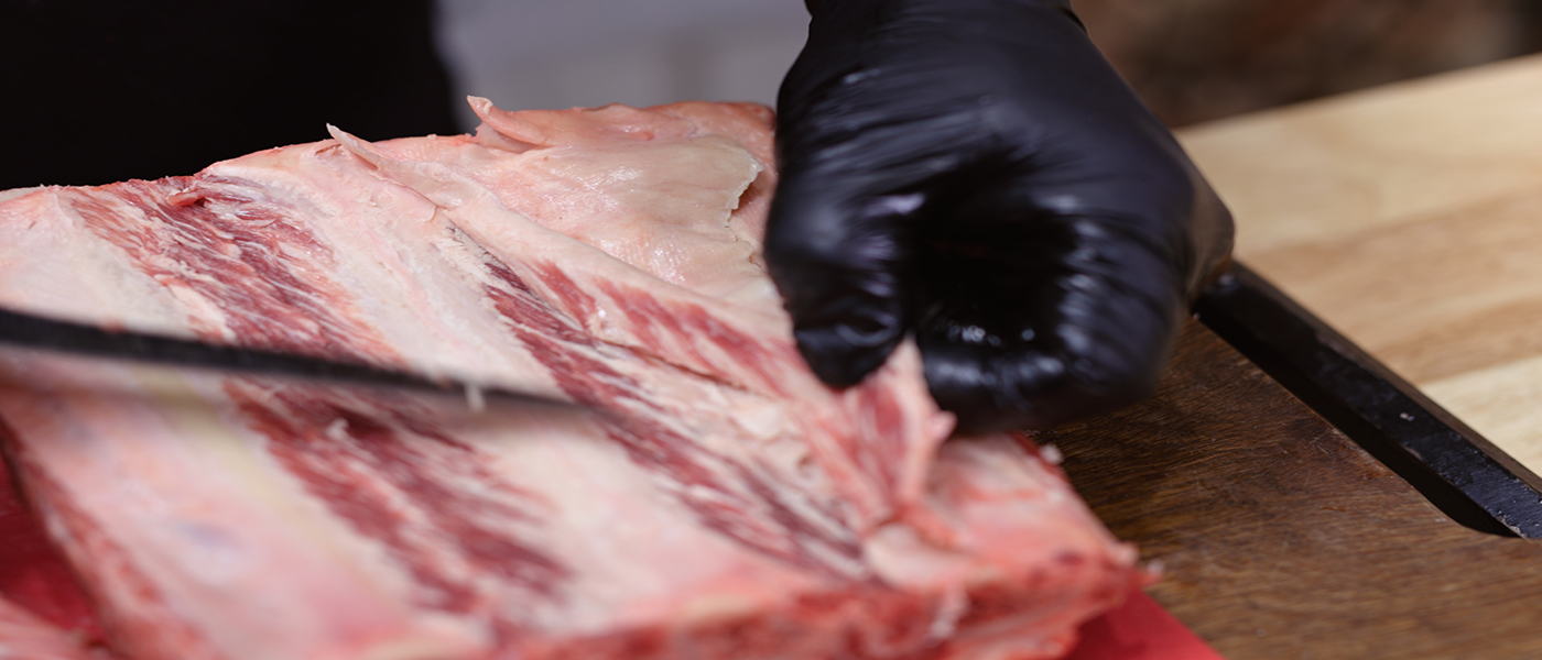 This image shows a man trimming the excess fat of short rib