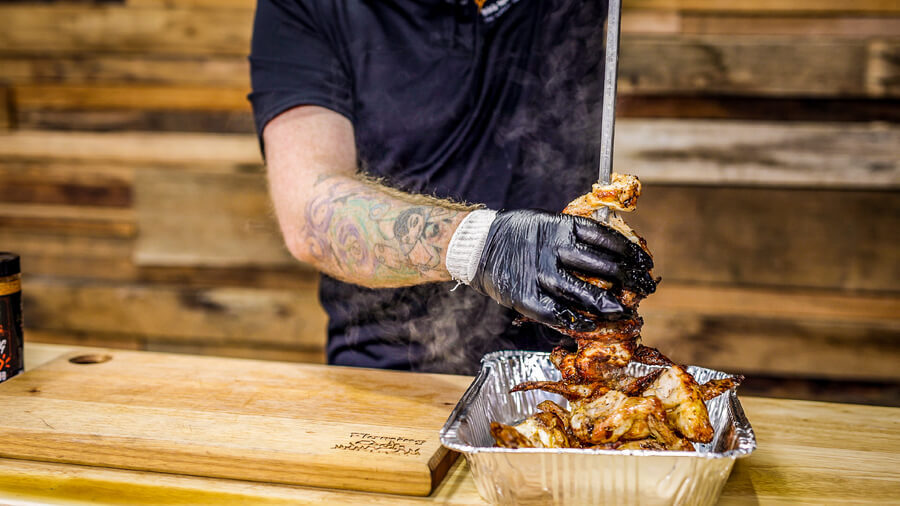 This image show a BBQ Chef using Black Nitrile gloves to protect his hands while removing chicken from a skewer. 