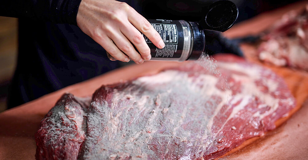 This image shows the brisket being seasoned with Kosmos Q ‘The Best’ Prime Steak
