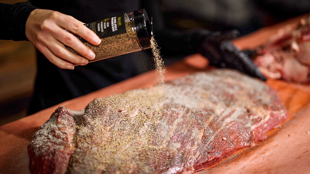 This image shows brisket being seasoned with Flaming Coals Bovine Espresso Rub