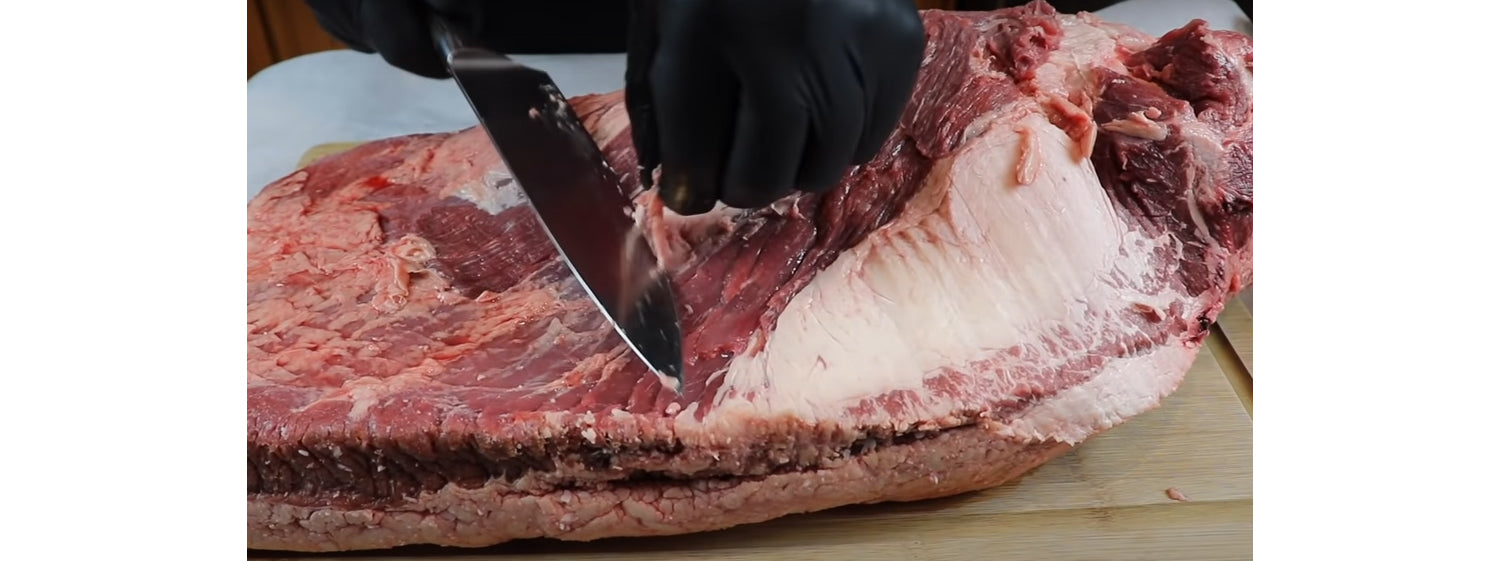 This image shows a man trimming the fat of the brisket and preparing to cook it is a Kettle BBQ while following the easy Brisket Recipe