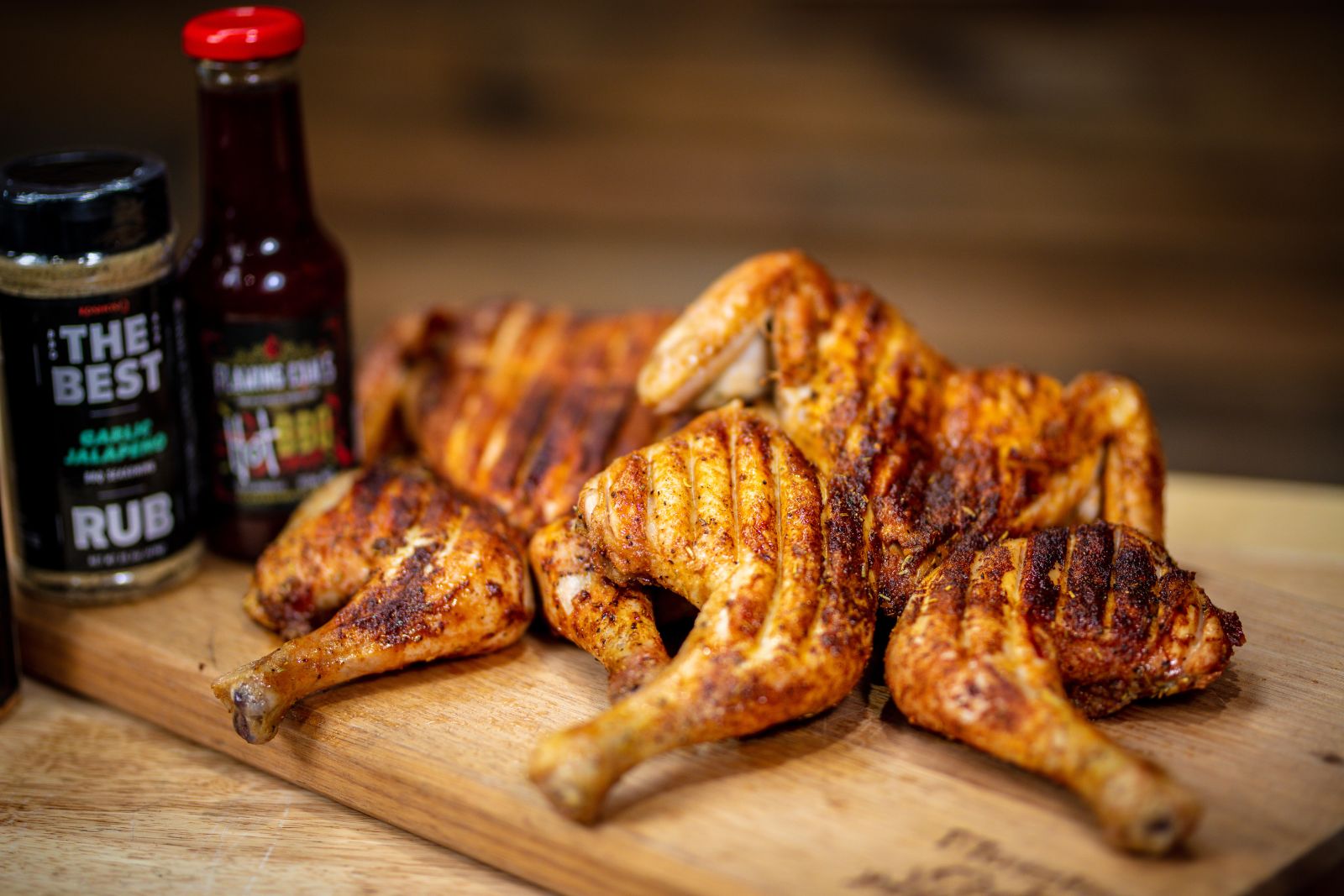 Perfectly grilled butterflied chicken on a wooden board with seasoning and barbecue sauce bottles in the background, ready to serve.