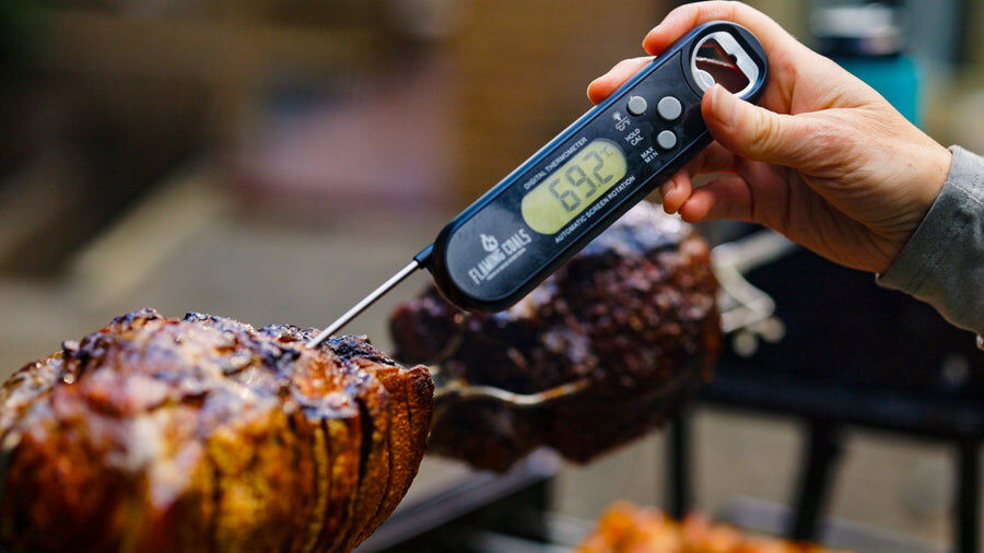 Digital BBQ thermometer with rotating probe measuring temperature of roast meat on a spit rotisserie
