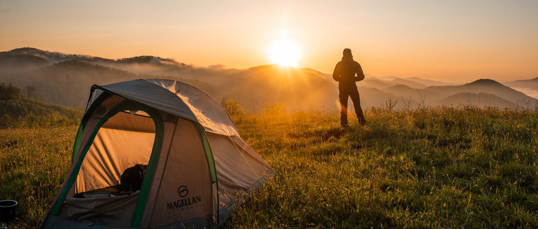 This image shows man watching a beautiful sunset during camping