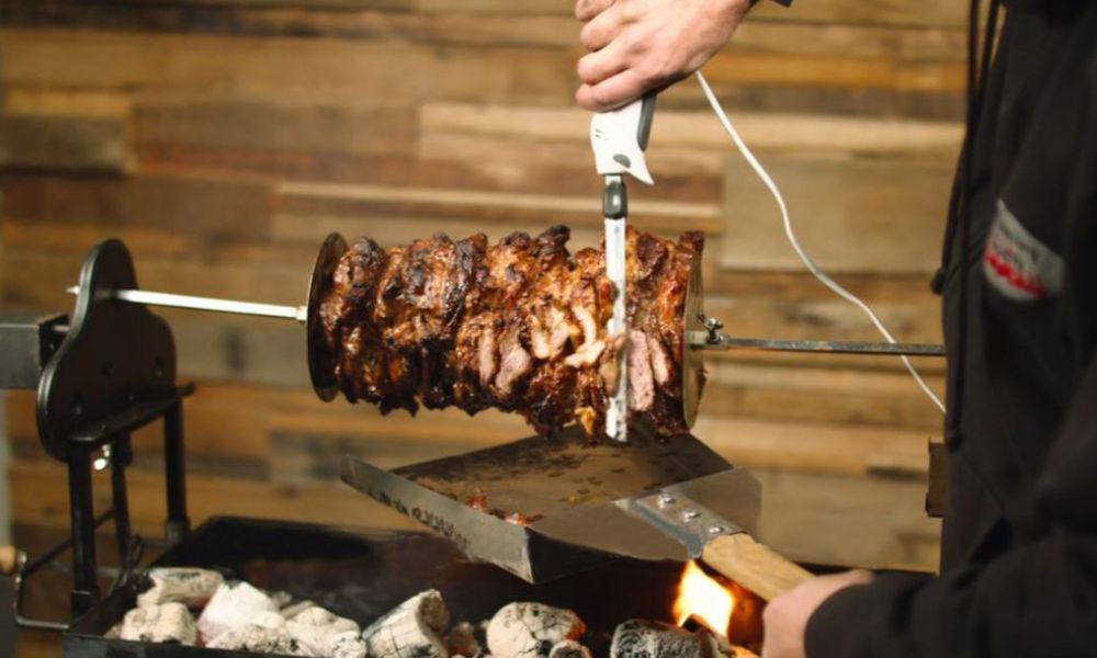 Carving gyros on the spit – electric carving knife slicing perfectly cooked rotisserie meat.