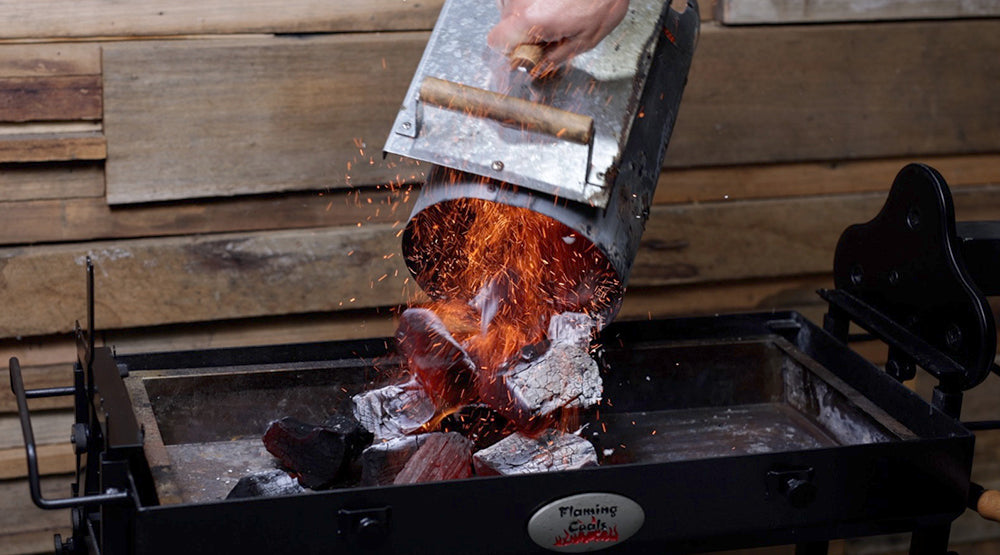 Charcoal chimney starter pouring lit coals into a Flaming Coals spit roaster charcoal pan.