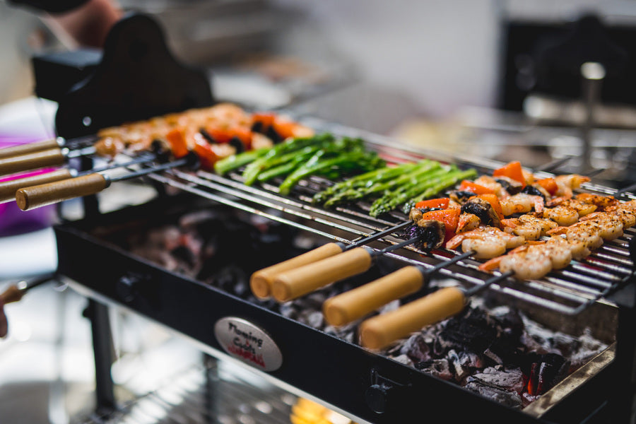 This is an image of a flaming coals charcoal BBQ in use. You can see prawns and greens being cooked over charcoal