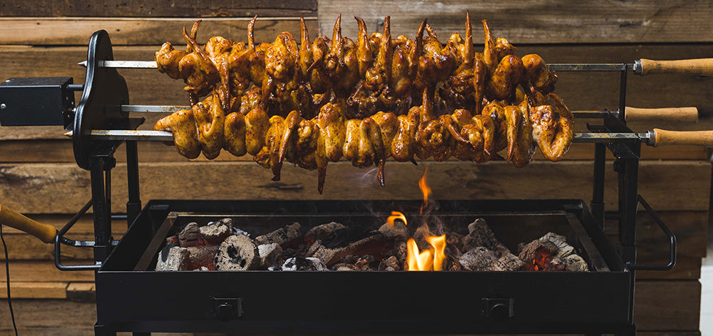 Chicken wings roasting on twin rotisserie skewers over charcoal on a Cyprus Spit.