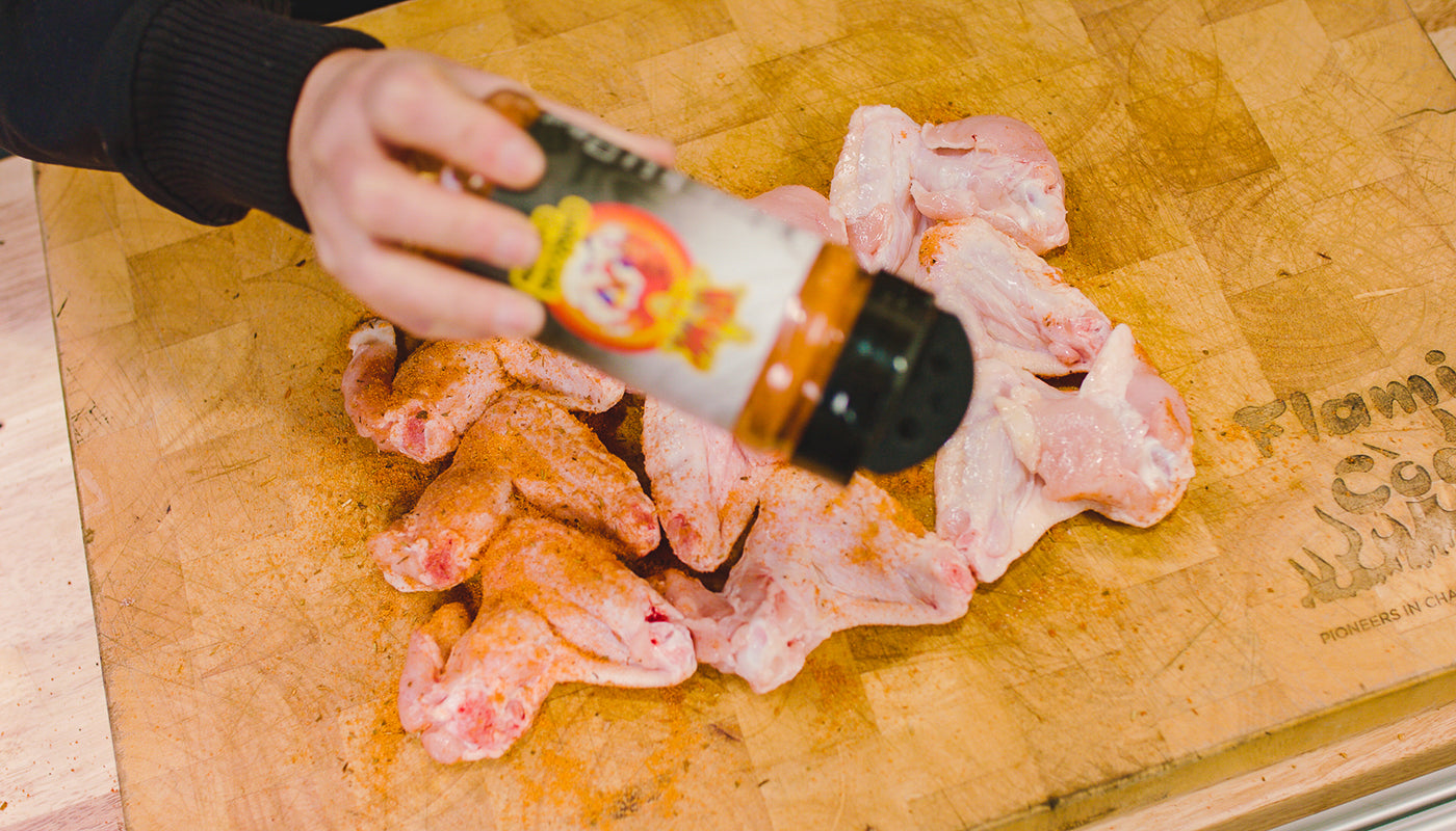 Raw chicken wings being seasoned with BBQ rub on a wooden chopping board before cooking
