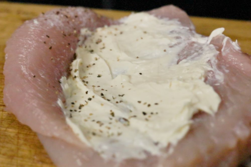 Raw butterflied chicken breast spread with seasoned cream cheese filling, ready to be rolled and wrapped for stuffing