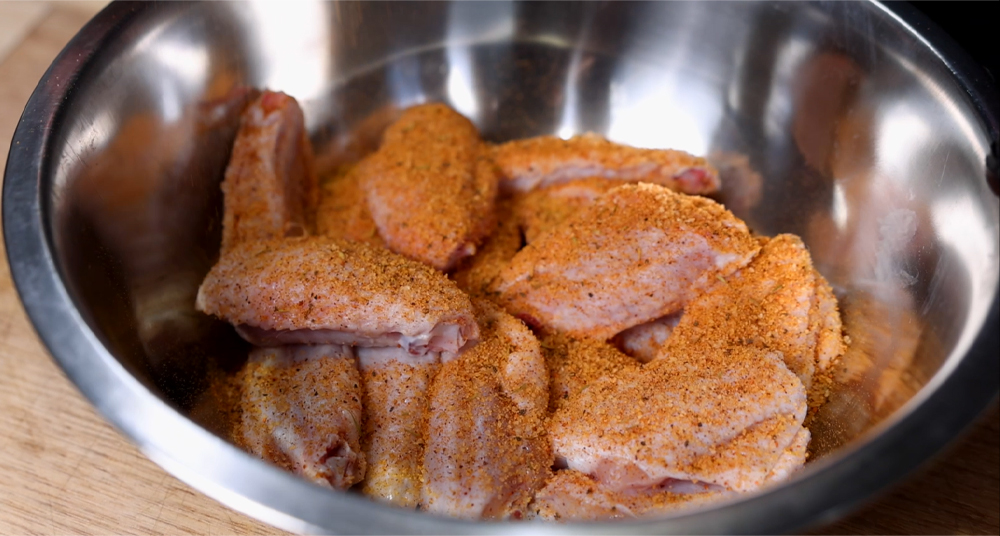 This image shows chicken wings being seasoned with Boomas Clucked and Plucked BBq Rub
