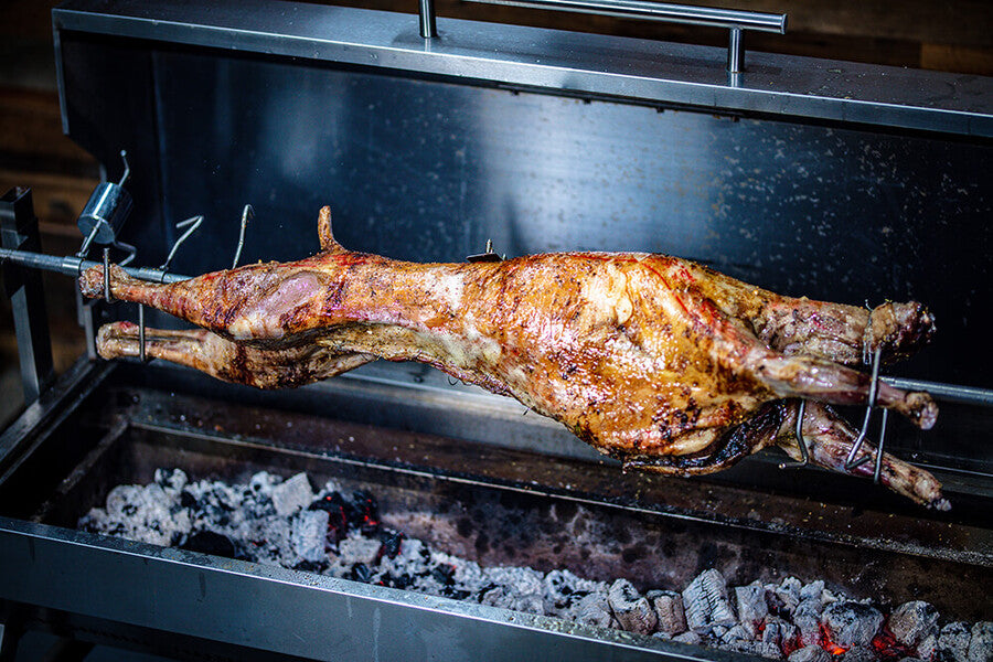Spit roast lamb on rotisserie with counter balance weight – cooking over charcoal evenly spread for better results