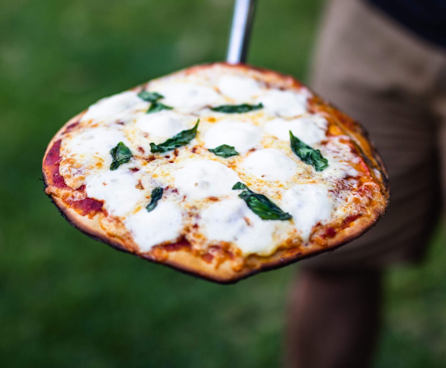 Freshly cooked Margherita pizza with melted mozzarella and basil on a pizza peel outdoors.