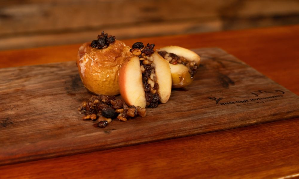 Baked apples stuffed with dried fruits and nuts, served on a rustic wooden board, cooked in a wood-fired pizza oven.