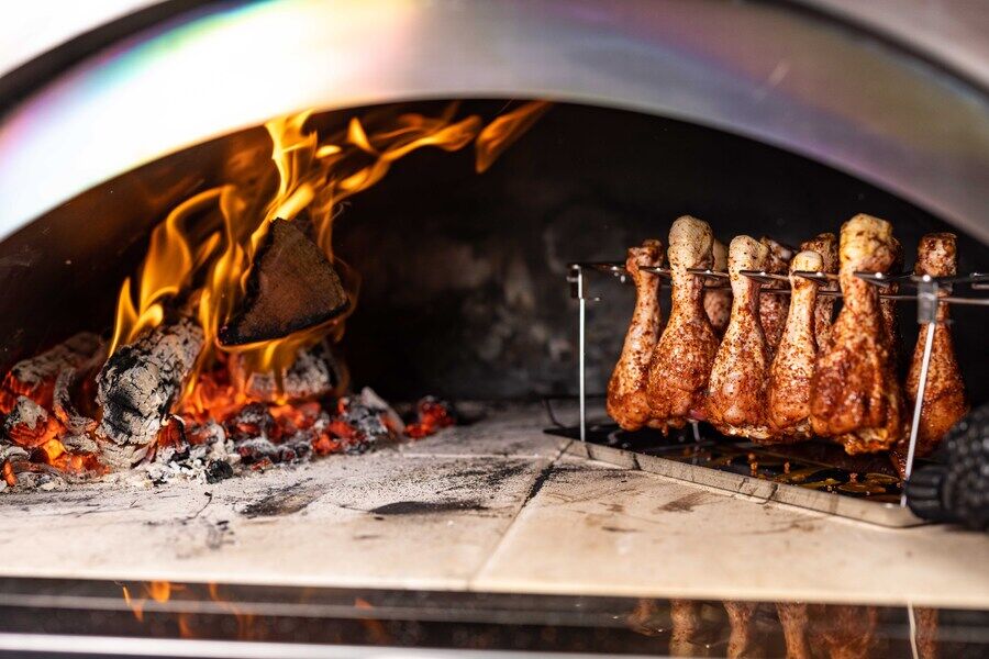 Chicken drumstick rack cooking upright chicken legs inside a wood-fired pizza oven
