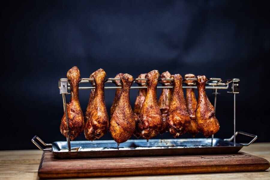 Chicken drumstick rack holding evenly cooked chicken drumsticks on a barbecue with drip tray underneath