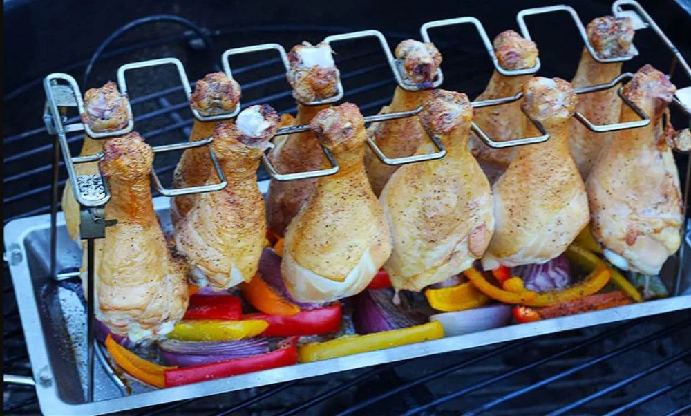Chicken Drumstick Cooking Rack holding multiple chicken legs upright over sliced vegetables on a BBQ grill.