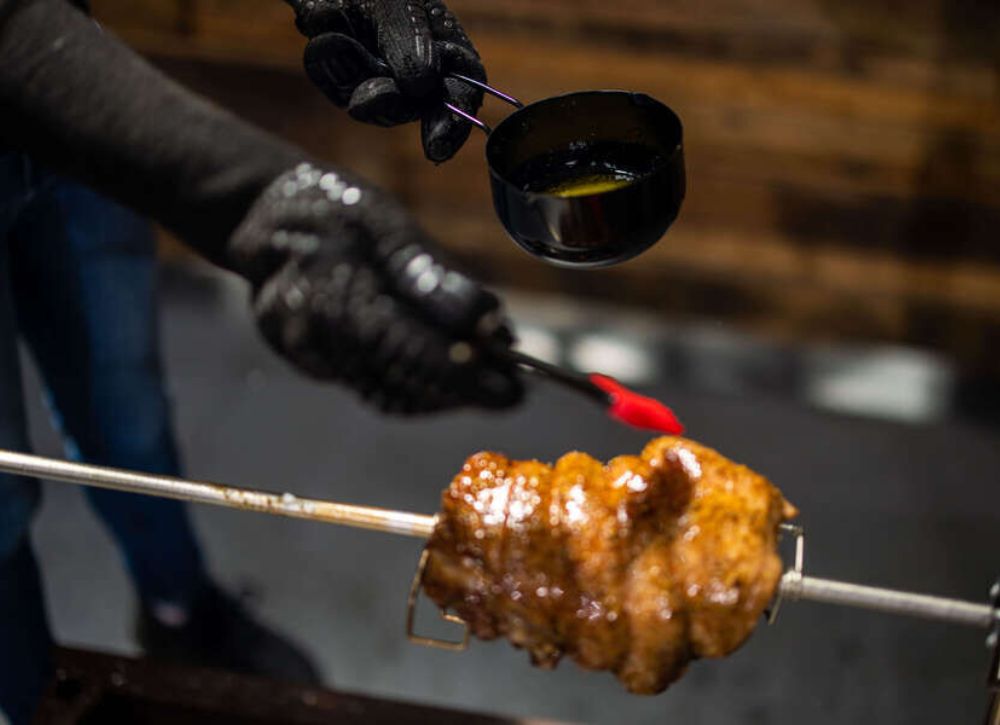 BBQ Sauce Pot with Basting Brush being used to coat meat on a rotisserie spit, with sauce applied using a red silicone brush.