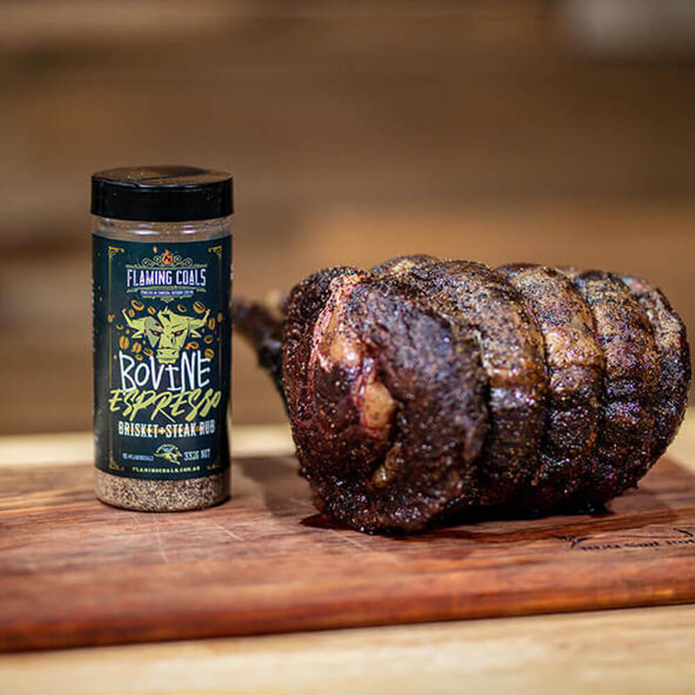 Flaming Coals Bovine Espresso Brisket and Steak Rub with a seasoned and roasted prime rib on a wooden board.