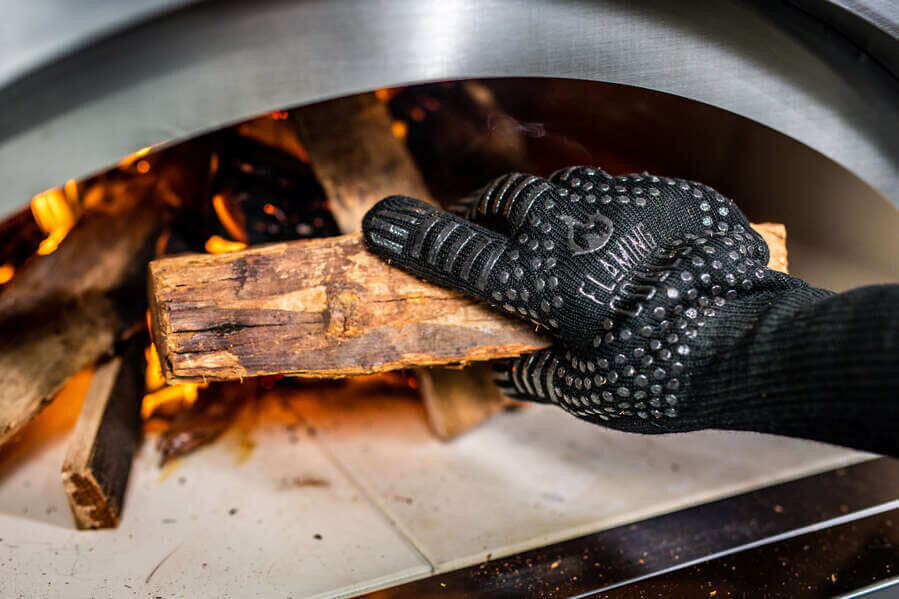heat resistant bbq glove placing wood into wood fired oven with flames for safe cooking