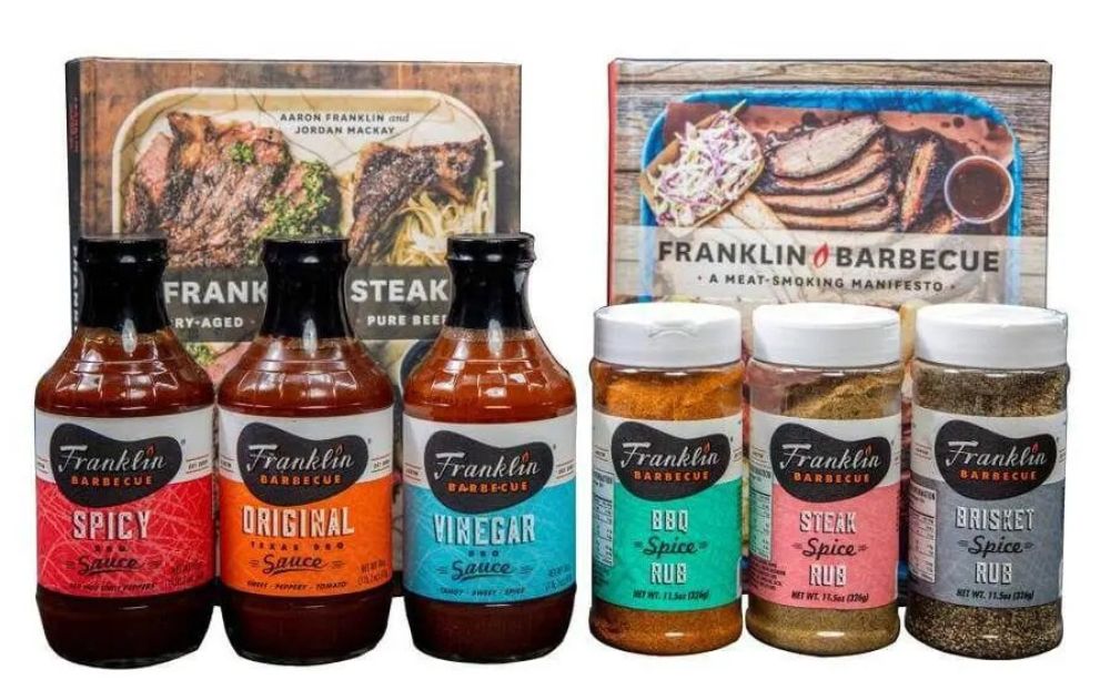 The image is the cover of the Franklin Steak BBQ book, featuring dry-aged, live-fired, and pure beef steaks. The cover shows a platter with cooked steak cuts topped with chimichurri and a side of noodles, accompanied by a bowl of green sauce. The book is authored by Aaron Franklin and Jordan Mackay.