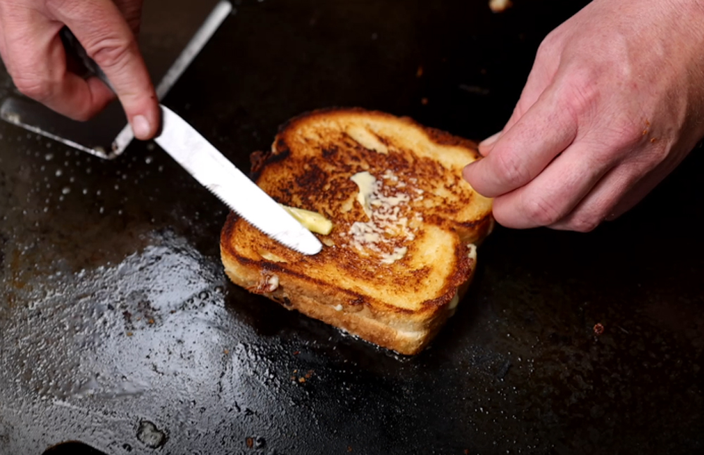 This_image_shows_a_butter_being_added_to_the_grilled_sandwich