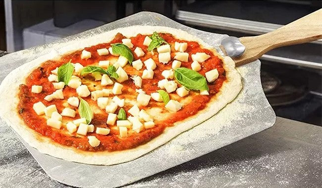 Uncooked pizza topped with tomato sauce, mozzarella and fresh basil on a floured pizza peel.