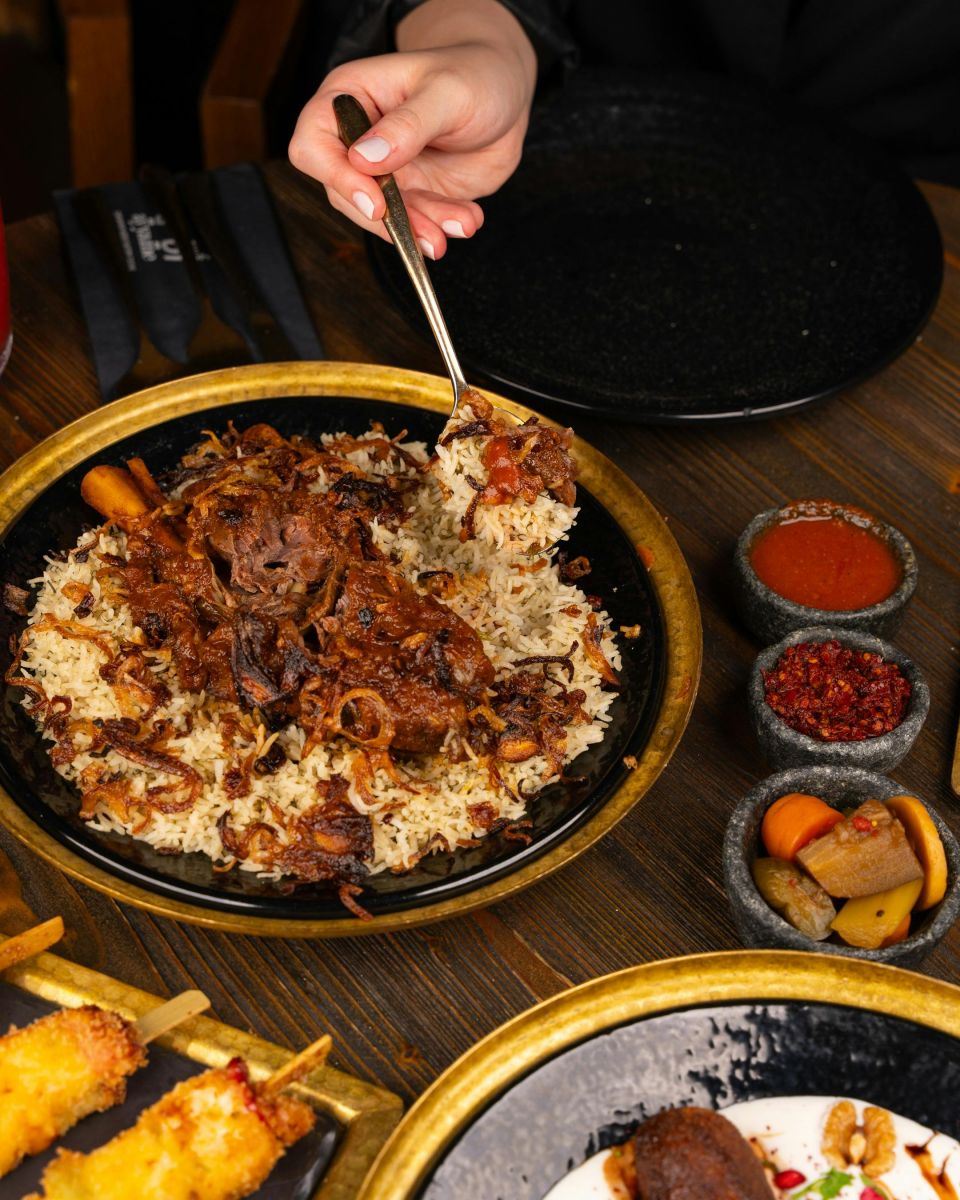 Plate of fried rice topped with leftover BBQ meat and caramelised onions, served with side sauces and pickled vegetables. Photo by pexels-ali-dashti