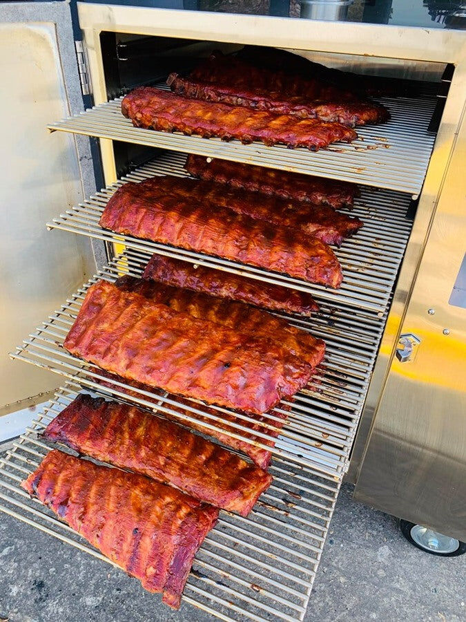 Multiple racks of ribs cooking inside a stainless steel gravity-fed smoker.