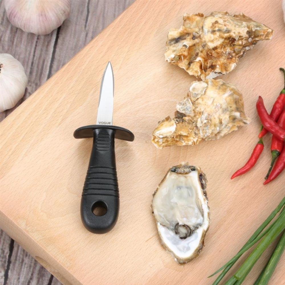 Vogue Oyster Knife with stainless steel blade and black ergonomic handle displayed on a wooden board beside fresh oysters, garlic, and red chillies.