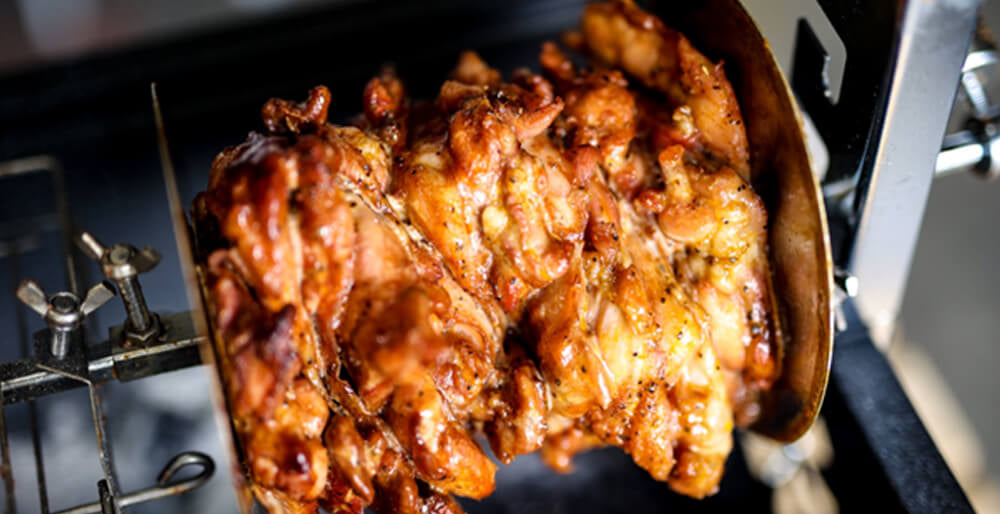 Close up of stacked gyros meat rotating on a spit between holding discs, showing crispy caramelised outer layer.