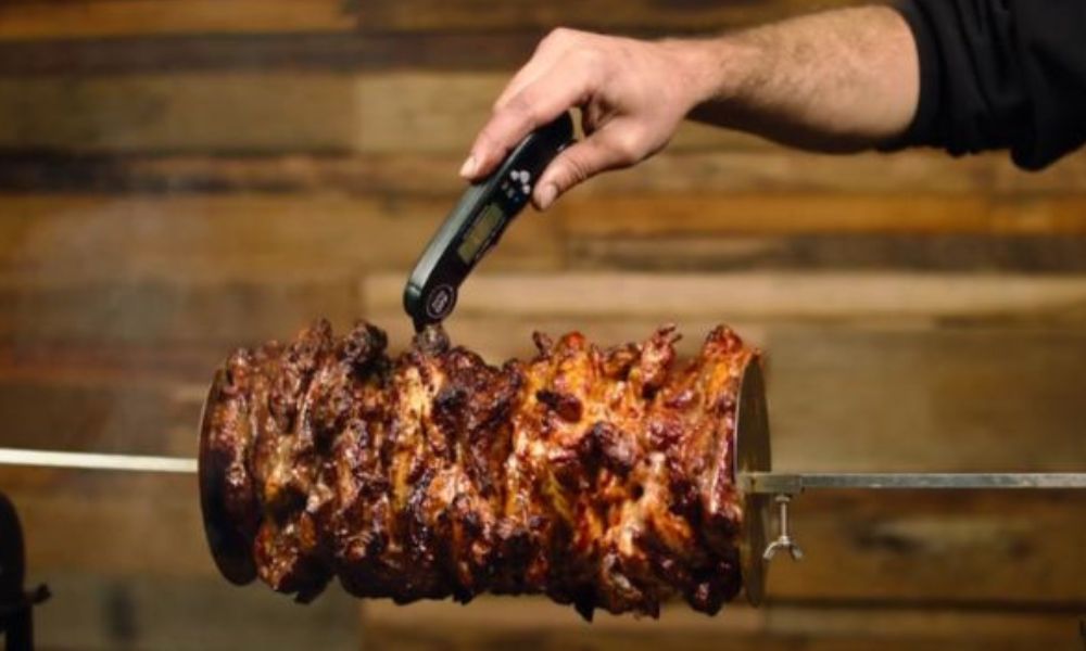 Checking internal temperature of rotating gyros meat on a spit using a digital meat thermometer.