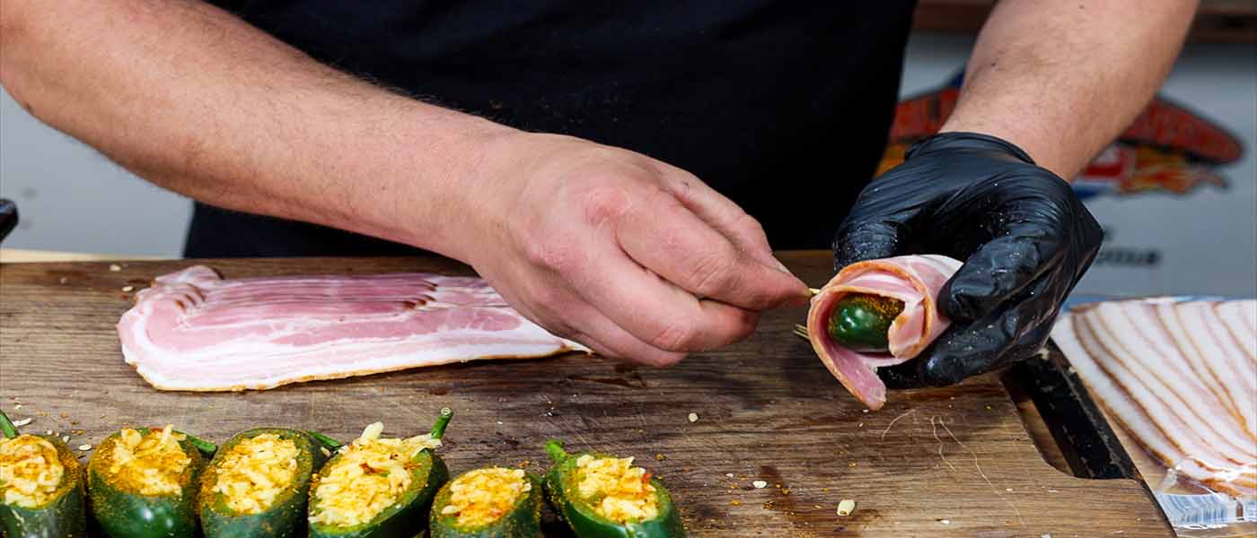 This image shows a man wrapping the Jalapeños with bacon