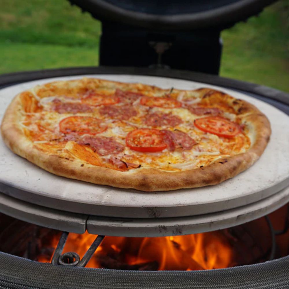 Classic Kamado Joe Ceramic Pizza Stone with a freshly baked pizza on top, showing even cooking on the stone over a glowing fire in the Kamado grill.