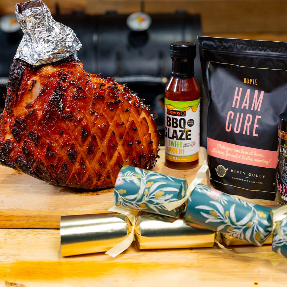 Sweet apricot glazed Christmas ham displayed with Kosmos BBQ Glaze, Misty Gully Ham Cure, and festive crackers.