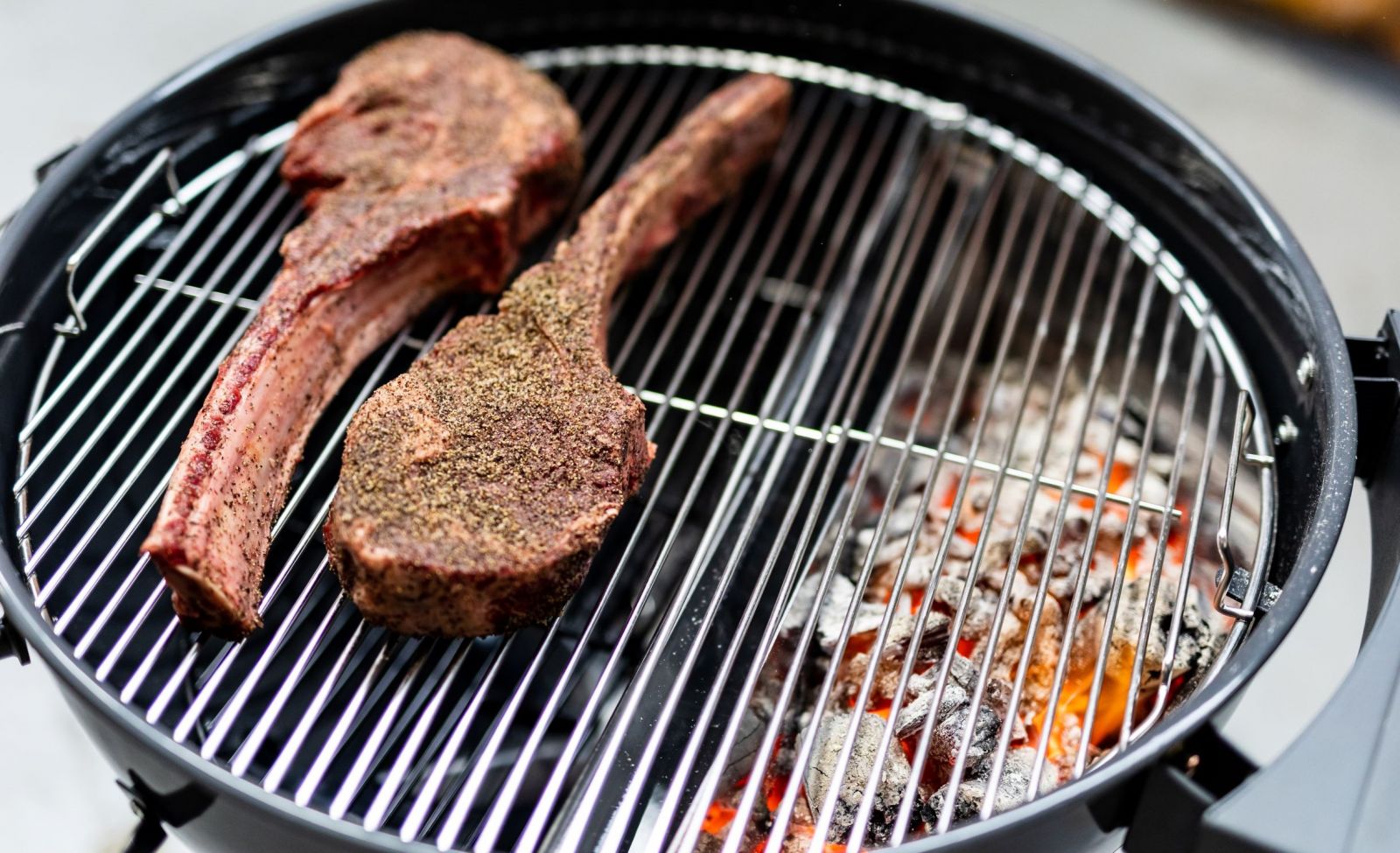 This image shows the Slow n Sear Kettle BBQ reverse searing some steaks with the use of the SnS charcoal holder