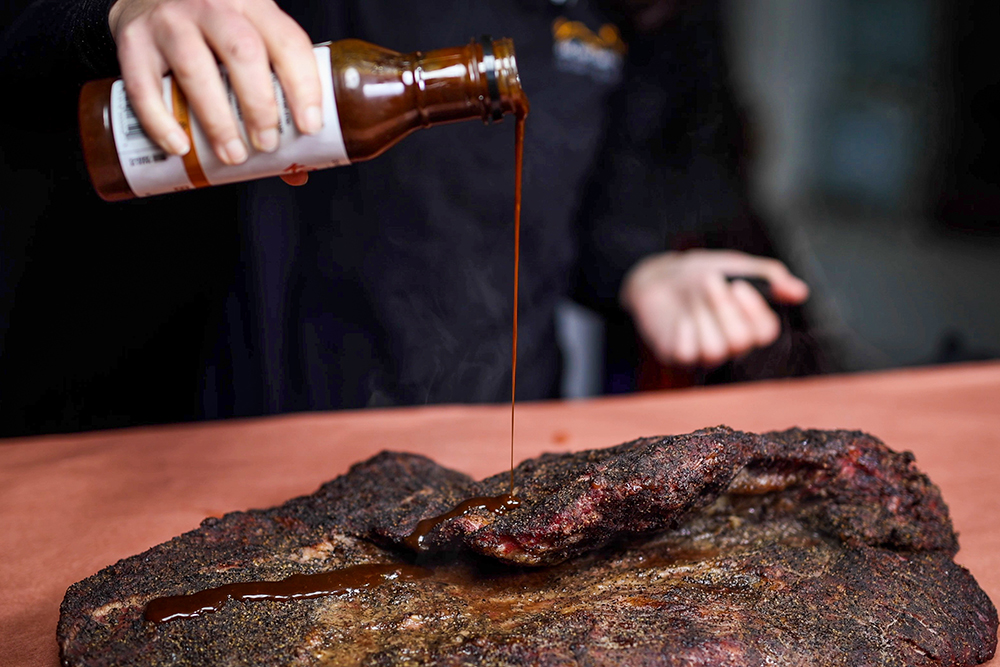 This image shows Brisket being seasoned with Kosmos Q Sauce