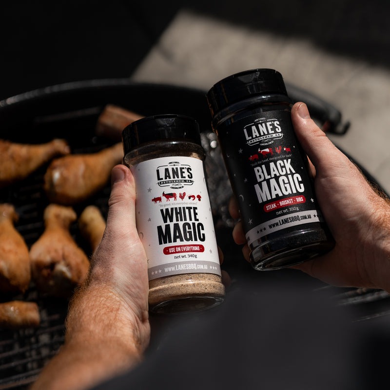 Lane’s Black Magic BBQ rub seasoning a steak with dark bark on charcoal grill