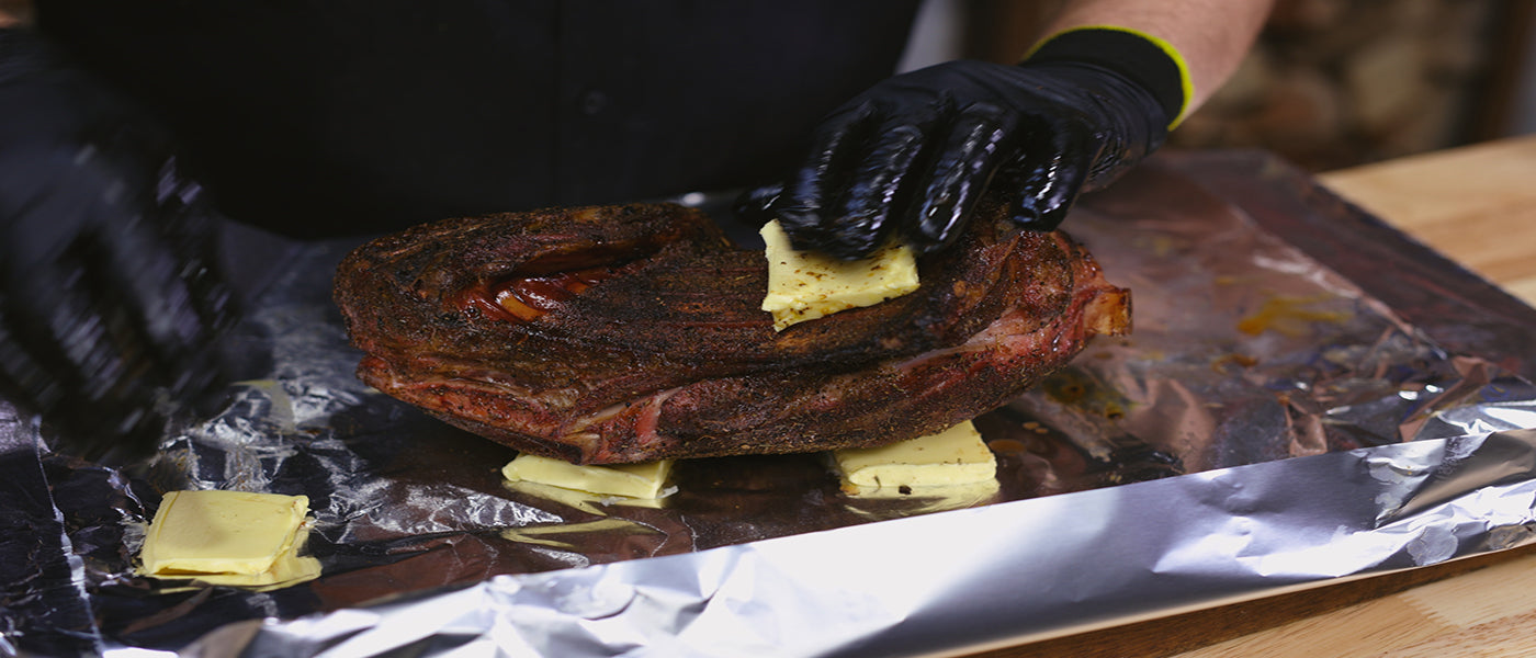 This image shows a man wrapping the lamb shoulder in the foil with butter. 