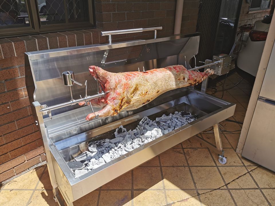 This picture shows a lamb being cooked on a Flaming coals hooded spit roaster over charcoal