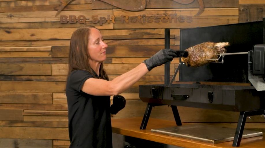 Checking the internal temperature of a leg of lamb cooking on a rotisserie spit using a digital thermometer.