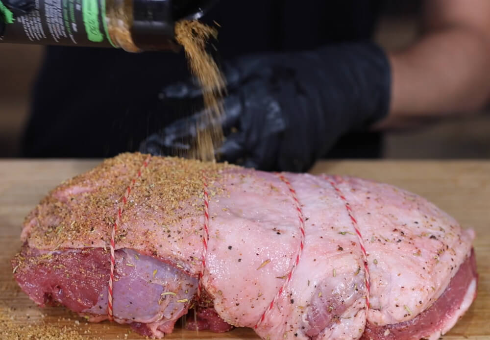 This image shows leg of lamb being rub with Boomas Sheard and Seard BBQ Rub