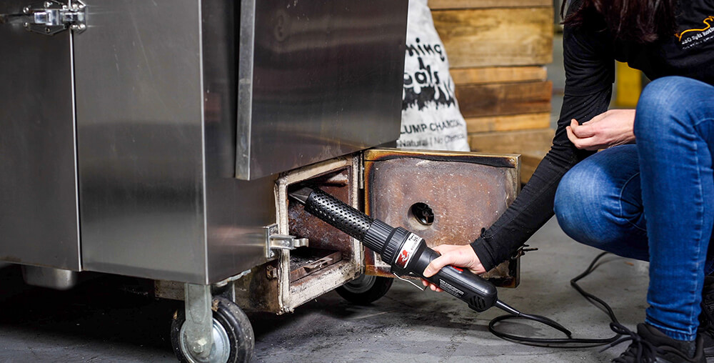 This image shows charcoal starter wand being used to start a fire in the Gravity Feed Smoker